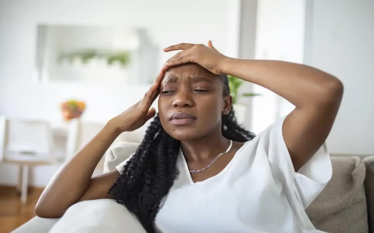 How to Manage Stress and Anxiety: Natural Remedies and Techniques 1 portrait young black girl sitting couch home with headache pain beautiful woman suffering from chronic daily headaches sad woman holding her head because sinus pain