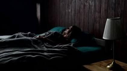 Inside-Out Care: Why True Beauty Sleep Starts with Stress Relief 8 A woman sleeping peacefully on comfortable pillows in a cozy dark bedroom with warm lamp lighting