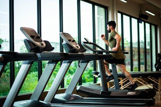 Discover Century City: Cape Town's Premier Mixed-use Development 14 Young man workouts on treadmill in modern gym with large windows and natural light.