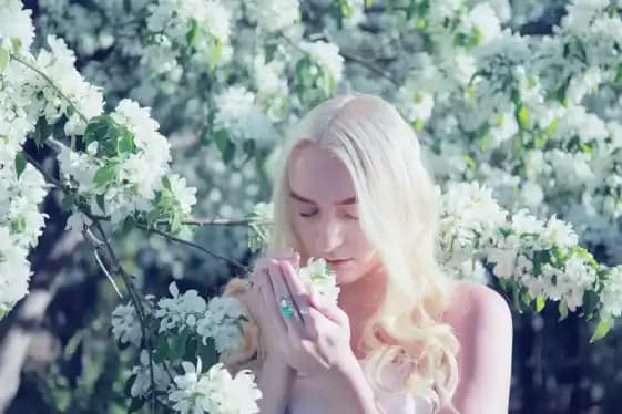 Natural Skin Care: Achieve Radiant Skin with PrimeBiome 10 Woman with blonde hair, hands clasped together, and a thoughtful expression, surrounded by a profusion of white flowers.