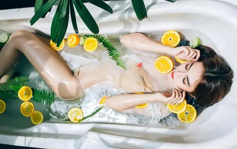 Natural Skin Care: Achieve Radiant Skin with PrimeBiome 12 Woman in a bathtub filled with water, citrus slices, and greenery.